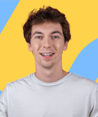 Young man with brown, wavy hair and a white t-shirt smiling against a yellow and blue abstract background.