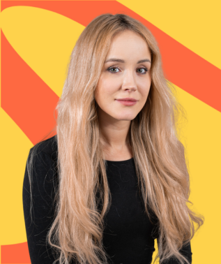 Young woman with long, wavy blonde hair wearing a black top against a yellow and orange abstract background.