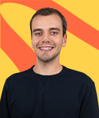 Smiling young man with dark hair wearing a navy blue sweatshirt against a yellow and orange striped background.