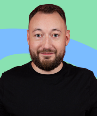 Man with short brown hair and a full beard smiling against a light green and blue abstract background.