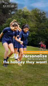 Dwie uśmiechnięte dziewczyny w granatowych strojach piłkarskich trzymają się za ręce podczas ćwiczeń na zielonej murawie.