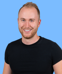 Młody, uśmiechnięty mężczyzna o jasnej karnacji i krótkich włosach, ubrany w czarną koszulkę, na jasnoniebieskim tle.