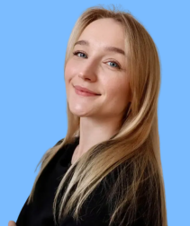 Młoda kobieta o jasnych włosach i niebieskich oczach uśmiecha się na tle jasnoniebieskim.