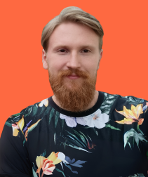 Mężczyzna z jasnymi włosami i rudą brodą w czarnej koszulce w tropikalne wzory na pomarańczowym tle.