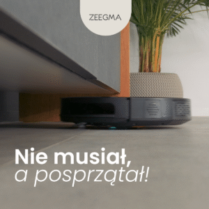 Czarny robot sprzątający Zeegma przejeżdża pod niską szafką na szarym kafelkowym podłożu. W tle doniczka z rośliną.