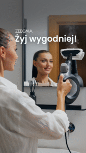 Kobieta w białej koszuli używa parownicy Zeegma do czyszczenia lustra w łazience. Widoczny jest dym pary.