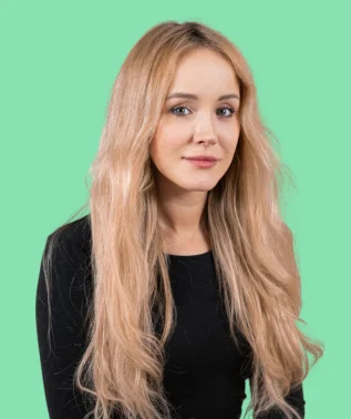 Young woman with long, light-colored hair, dressed in black, posing against a light green background.