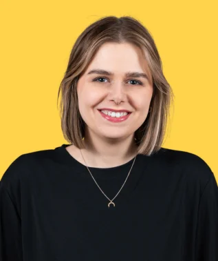 Young woman with fair skin and short blonde hair, smiling, wearing a black T-shirt, against a yellow background.