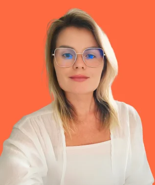 Woman with light-colored hair, wearing silver-rimmed glasses, dressed in white, against a solid orange background.