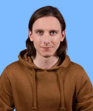 Young man with long, brown hair, wearing a brown hoodie, against a light blue background.