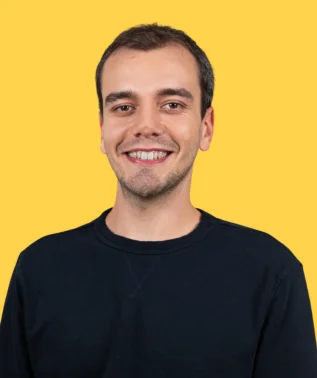 Young, smiling man with short, dark hair, wearing a navy blue sweatshirt, against a solid yellow background.