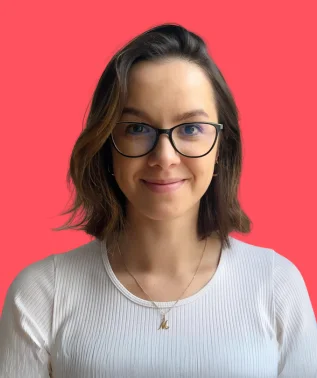 Portrait of a young woman wearing glasses, smiling, against a light pink background."