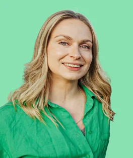 Smiling blonde woman wearing a green shirt, against a solid light green background.