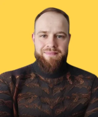 Man with fair skin, short hair, and a full red beard, wearing a black patterned turtleneck, against a yellow background.