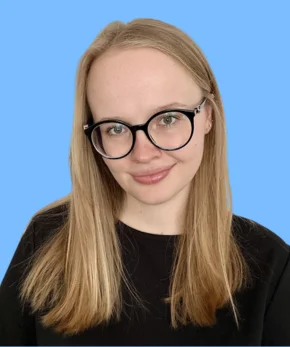 Young woman with long blonde hair and round black glasses smiling against a solid blue background.