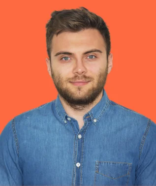 Young man with stubble and blue eyes, wearing a denim shirt, against an orange background.