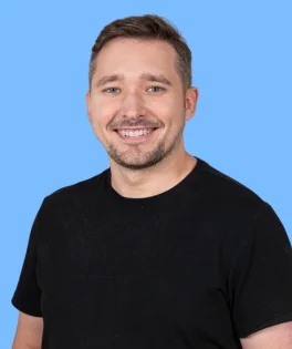 Smiling, fair-haired man wearing a black T-shirt, against a light blue background.