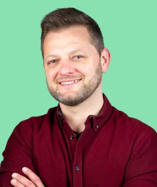 Smiling man with a short beard, wearing a burgundy shirt, against a light green background.