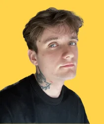 Young man with brown hair and blue eyes, wearing a black sweatshirt, with a bird tattoo on his neck, against a yellow background.