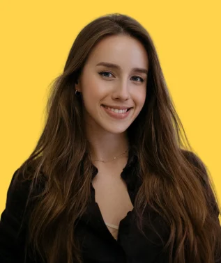 Young, smiling woman with long brown hair, wearing a black shirt, against a yellow background.