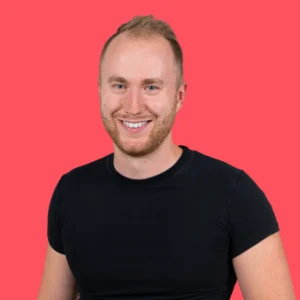 Smiling young man with short blonde hair and stubble, wearing a black T-shirt, against a bright red background.
