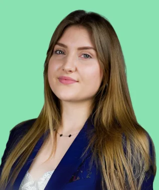 Young woman with long brown hair, wearing a navy blue blazer, smiling against a light green background.