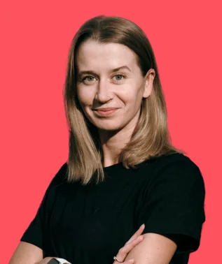 Portrait of a young woman with light hair, smiling, wearing a black T-shirt, against a bright red background.